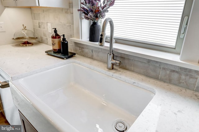 interior details featuring light stone counters, sink, and decorative backsplash