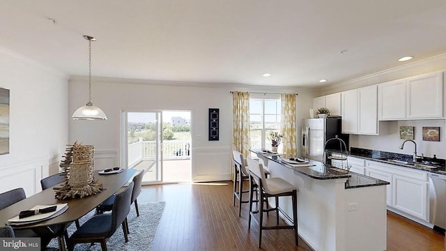 kitchen with sink, stainless steel appliances, crown molding, decorative light fixtures, and a center island with sink