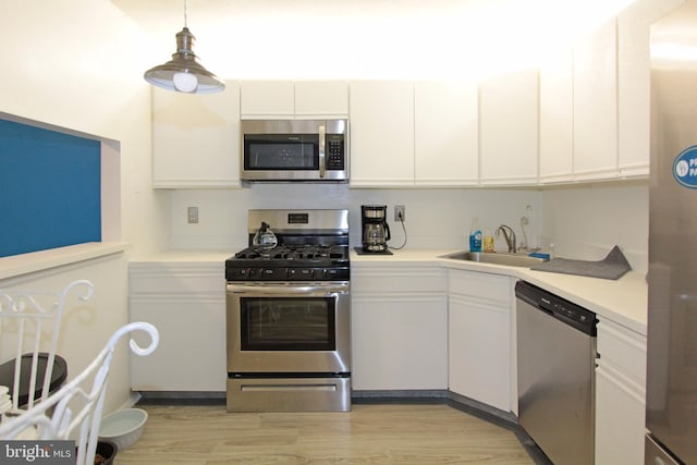 kitchen with pendant lighting, white cabinets, sink, appliances with stainless steel finishes, and light hardwood / wood-style floors