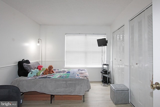 bedroom with a textured ceiling, two closets, and light wood-type flooring