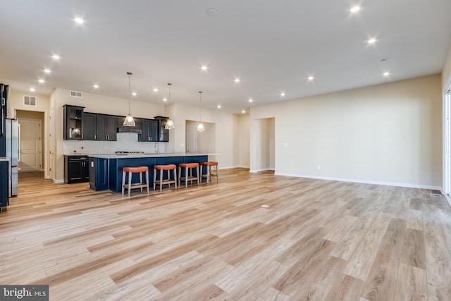 kitchen featuring a center island with sink, decorative light fixtures, light hardwood / wood-style floors, a breakfast bar area, and stainless steel refrigerator