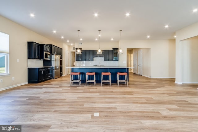 kitchen with light wood-type flooring, backsplash, a breakfast bar, pendant lighting, and a center island with sink