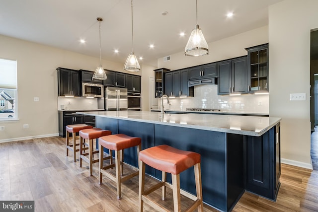 kitchen with a breakfast bar, stainless steel appliances, pendant lighting, light hardwood / wood-style flooring, and a large island