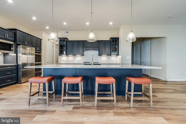 kitchen with stainless steel appliances, hanging light fixtures, a spacious island, and light hardwood / wood-style flooring