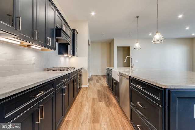 kitchen with stainless steel appliances, light hardwood / wood-style flooring, a large island with sink, pendant lighting, and exhaust hood