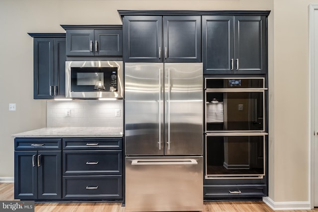 kitchen featuring tasteful backsplash, light stone counters, stainless steel appliances, and light hardwood / wood-style floors