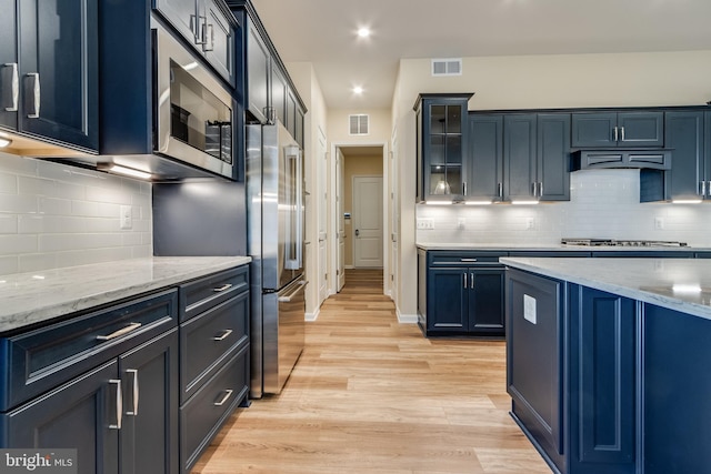 kitchen with backsplash, appliances with stainless steel finishes, blue cabinets, and light wood-type flooring