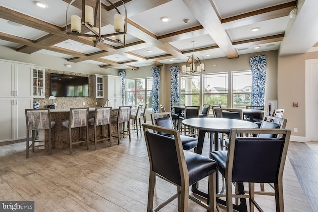 dining area with light hardwood / wood-style flooring, a wealth of natural light, a notable chandelier, and coffered ceiling