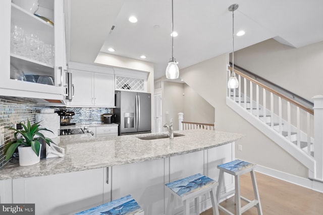 kitchen featuring pendant lighting, backsplash, white cabinets, sink, and stainless steel refrigerator with ice dispenser