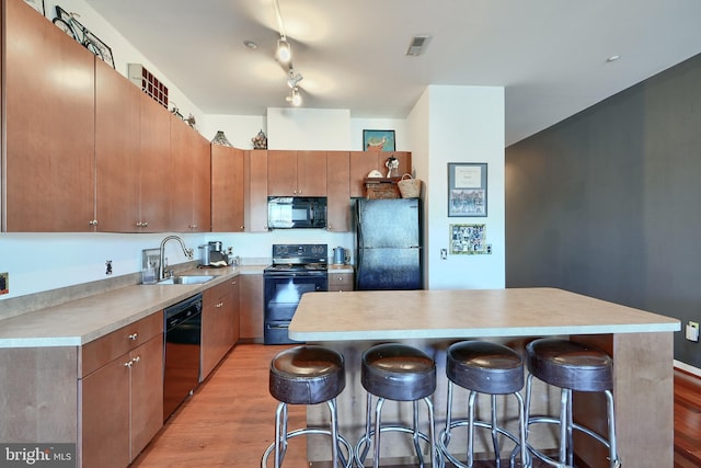 kitchen featuring sink, a center island, a breakfast bar area, black appliances, and light wood-type flooring