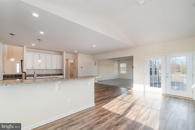 kitchen with decorative light fixtures, white cabinetry, french doors, a kitchen bar, and light stone countertops