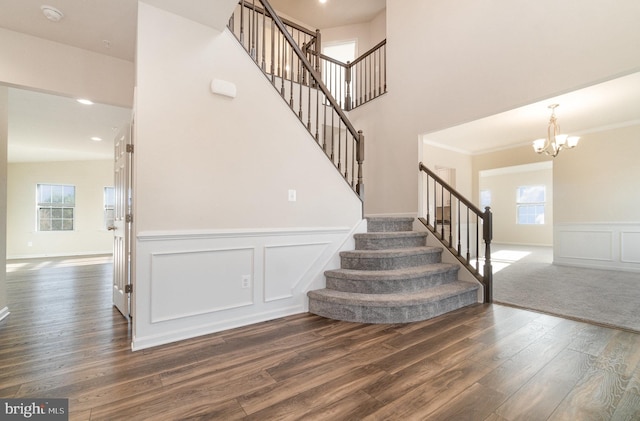 staircase with hardwood / wood-style floors, crown molding, and a notable chandelier