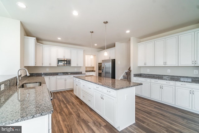 kitchen featuring dark stone countertops, stainless steel appliances, a center island, sink, and decorative light fixtures