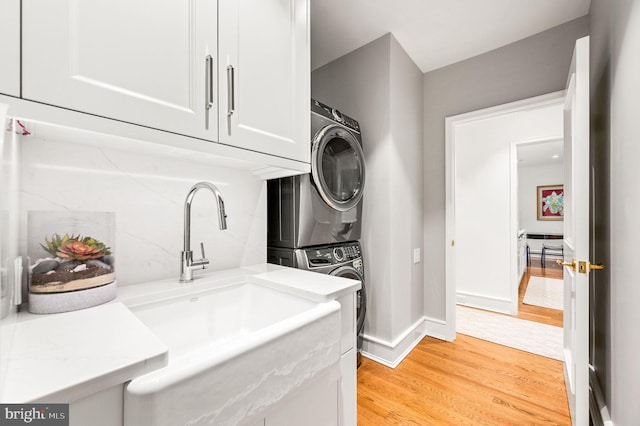 laundry area featuring stacked washer / drying machine, sink, light hardwood / wood-style floors, and cabinets