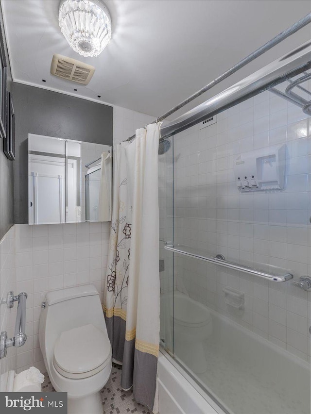 bathroom featuring tile patterned flooring, toilet, combined bath / shower with glass door, and tile walls