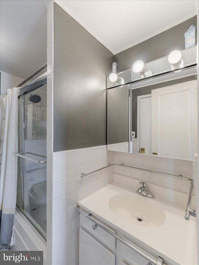 bathroom with vanity, toilet, a tile shower, and tile walls