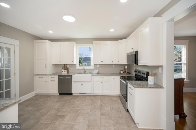 kitchen with white cabinets, stone countertops, stainless steel appliances, and sink