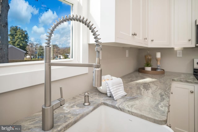 interior details with white cabinets, light stone counters, and sink