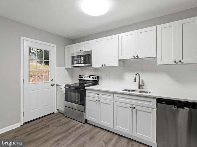 kitchen with backsplash, sink, white cabinetry, wood-type flooring, and stainless steel appliances