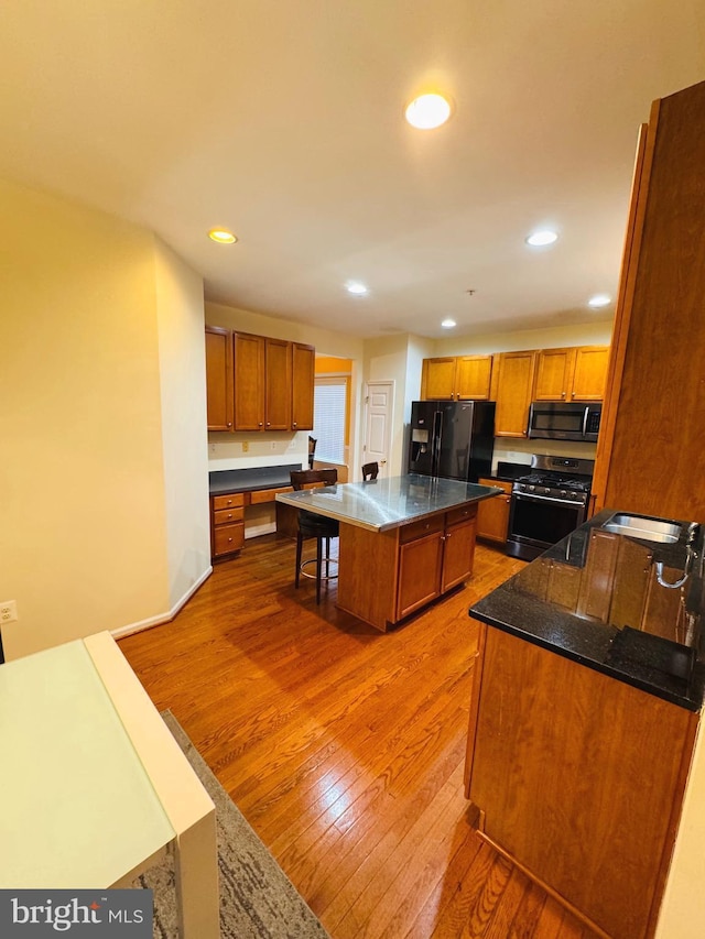 kitchen featuring a center island, hardwood / wood-style flooring, built in desk, appliances with stainless steel finishes, and a kitchen bar