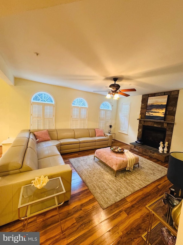 living room featuring hardwood / wood-style flooring, ceiling fan, and a stone fireplace