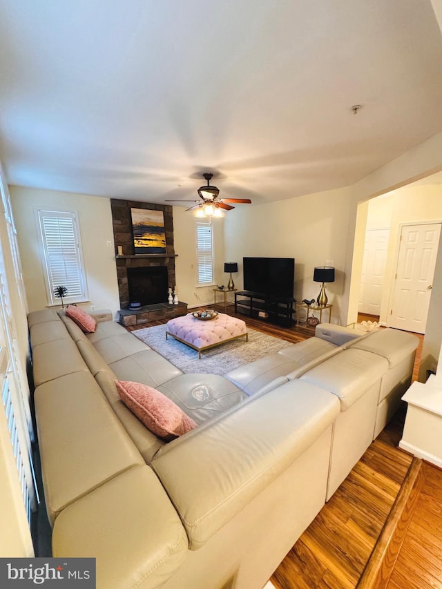 living room featuring hardwood / wood-style flooring, ceiling fan, and a stone fireplace