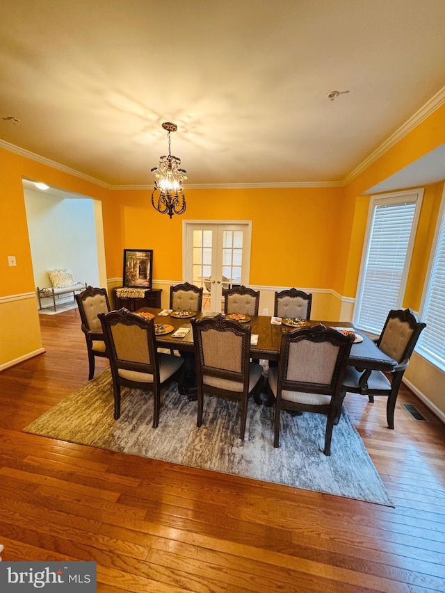 dining space featuring ornamental molding, wood-type flooring, french doors, and a notable chandelier