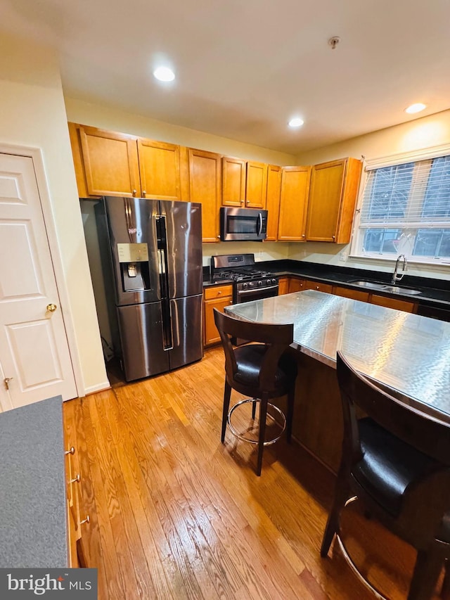 kitchen with a breakfast bar, sink, stainless steel appliances, and light hardwood / wood-style flooring