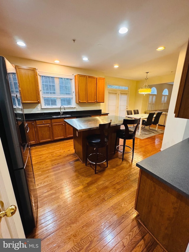 kitchen featuring sink, black fridge, light hardwood / wood-style flooring, pendant lighting, and a breakfast bar