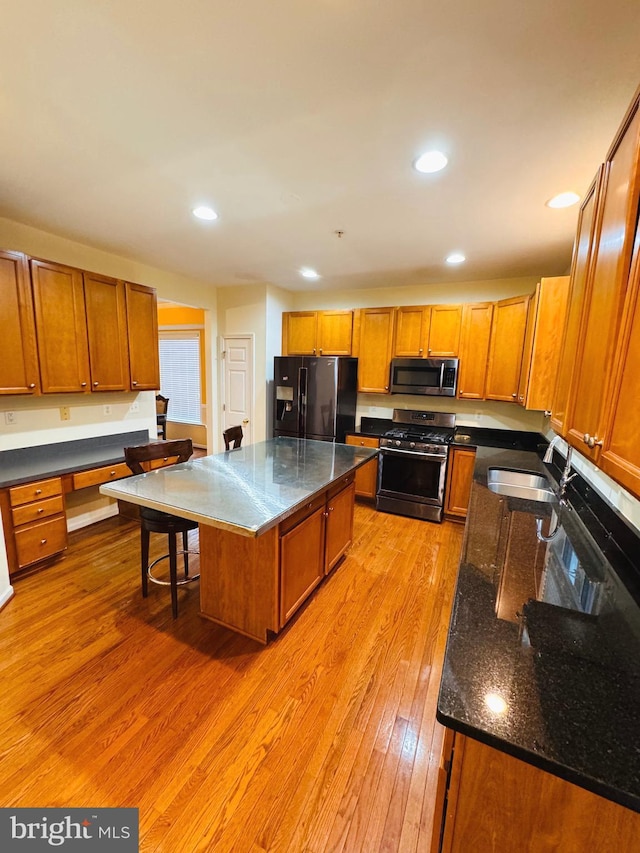 kitchen featuring sink, stainless steel appliances, dark stone counters, a kitchen island, and light wood-type flooring