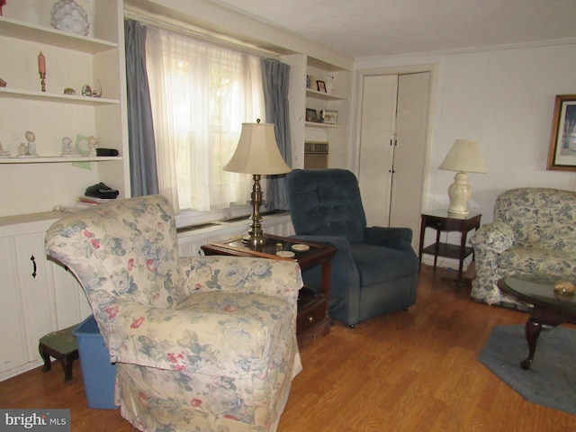 living area with built in features, ornamental molding, and hardwood / wood-style flooring