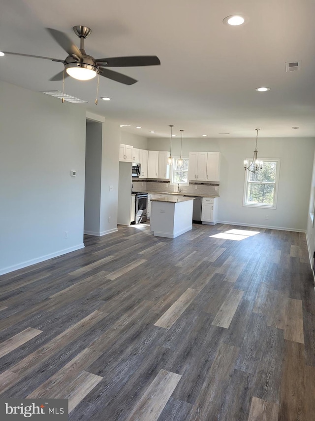 unfurnished living room with ceiling fan with notable chandelier and dark wood-type flooring