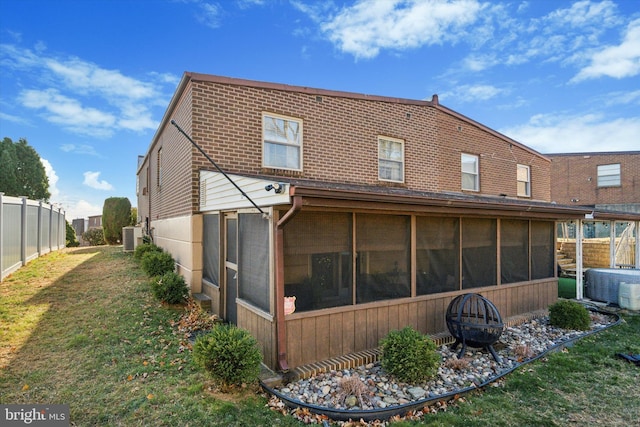 rear view of house with a sunroom, a yard, cooling unit, and an outdoor fire pit