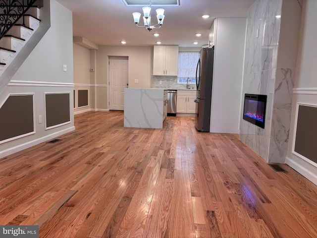 kitchen featuring stainless steel appliances, light stone counters, light hardwood / wood-style floors, a fireplace, and white cabinets