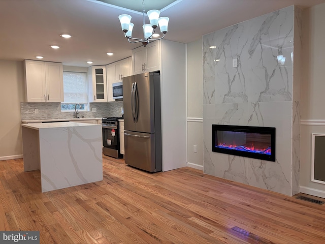 kitchen with a center island, hanging light fixtures, light wood-type flooring, white cabinetry, and stainless steel appliances