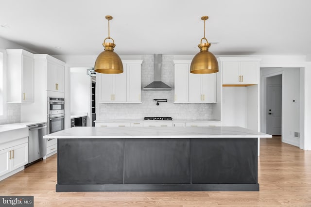 kitchen with stainless steel appliances, white cabinetry, decorative light fixtures, and wall chimney range hood