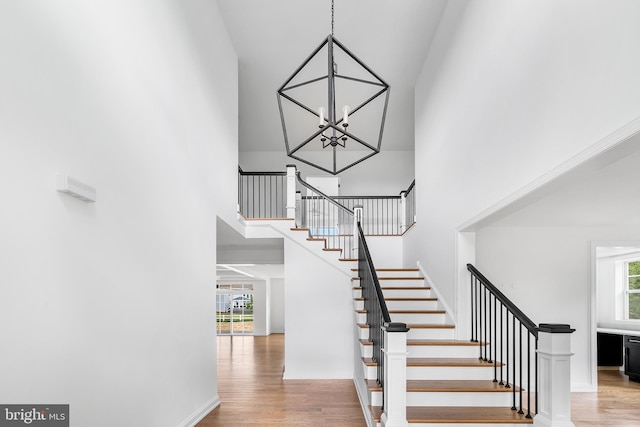 stairs featuring a towering ceiling, hardwood / wood-style flooring, and a notable chandelier