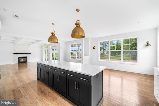 kitchen featuring light wood-type flooring, a large fireplace, light stone counters, and hanging light fixtures