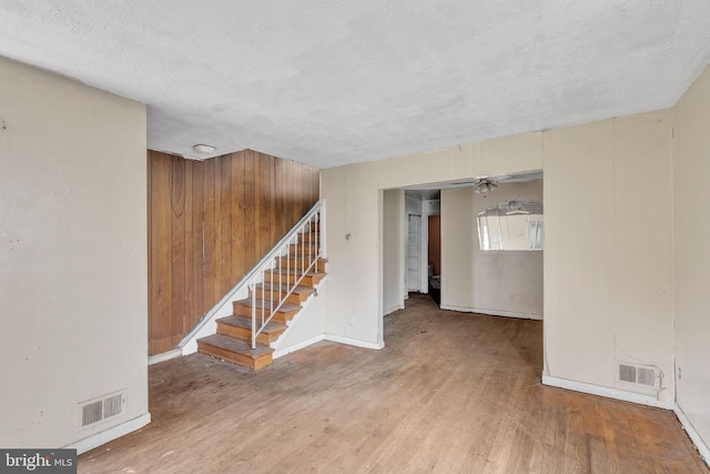 empty room featuring wood walls, hardwood / wood-style floors, ceiling fan, and a textured ceiling