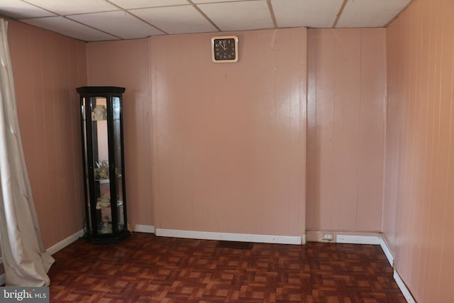 spare room with a paneled ceiling, dark parquet floors, and wood walls