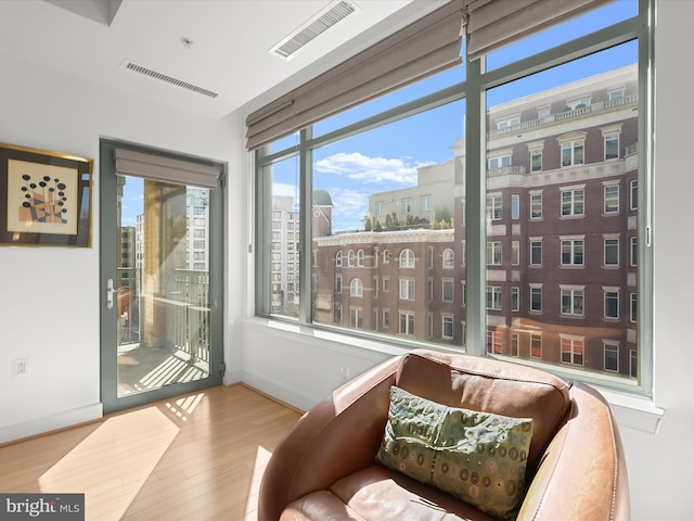 sitting room with a city view, wood finished floors, visible vents, and baseboards