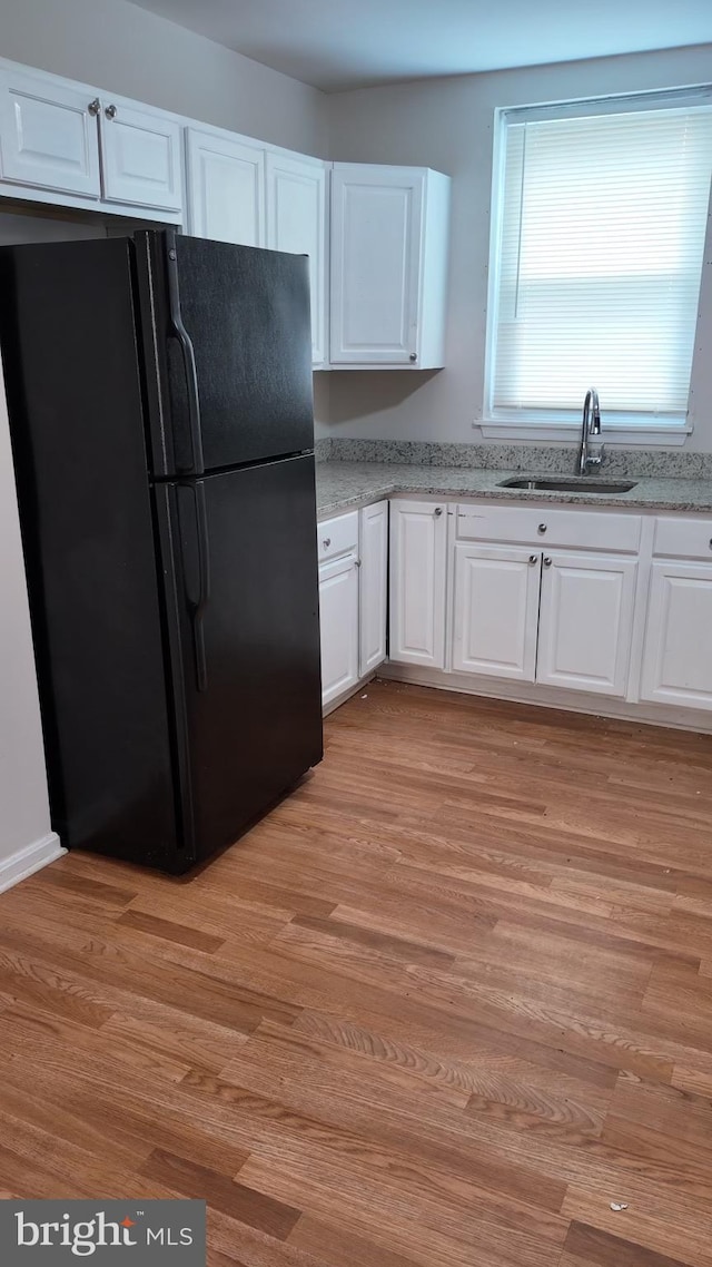 kitchen featuring white cabinetry, black refrigerator, light hardwood / wood-style floors, and sink