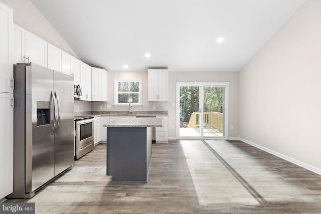 kitchen with lofted ceiling, a center island, white cabinetry, and appliances with stainless steel finishes