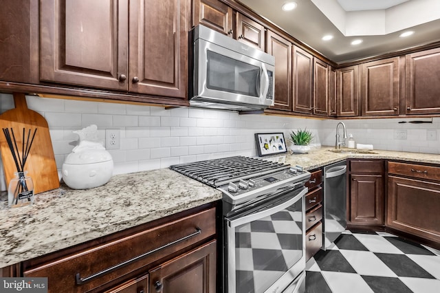 kitchen with dark brown cabinetry, sink, light stone counters, decorative backsplash, and appliances with stainless steel finishes