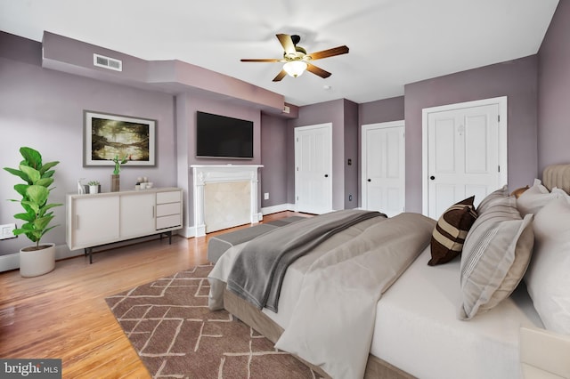 bedroom with multiple closets, ceiling fan, and wood-type flooring