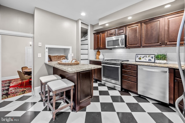 kitchen with appliances with stainless steel finishes, tasteful backsplash, dark brown cabinets, and a kitchen breakfast bar