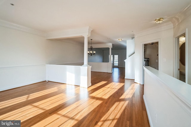 empty room featuring decorative columns, crown molding, a chandelier, and wood-type flooring