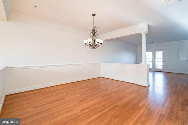 empty room featuring decorative columns, an inviting chandelier, ornamental molding, and light wood-type flooring