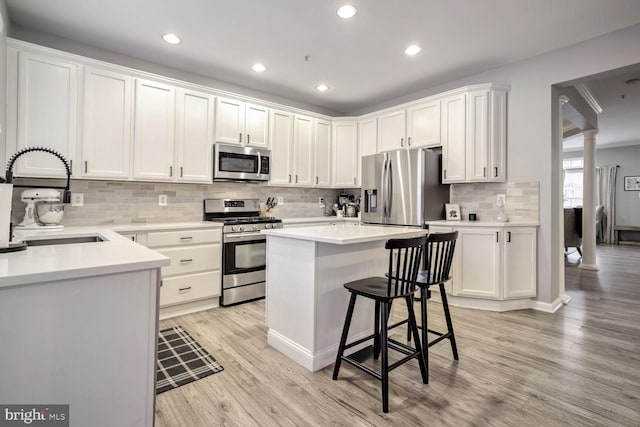 kitchen with white cabinetry, sink, stainless steel appliances, light hardwood / wood-style floors, and a kitchen island