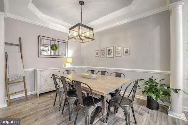 dining area with light wood-type flooring, decorative columns, a raised ceiling, and a notable chandelier